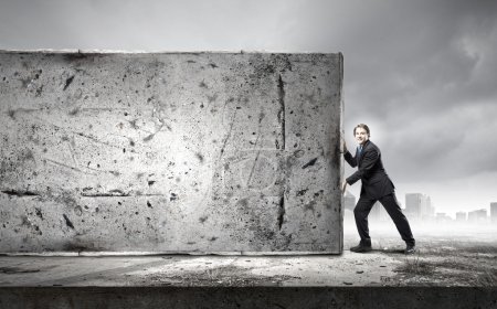 Foto de Joven empresario haciendo esfuerzo para mover la pared de piedra - Imagen libre de derechos