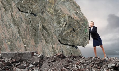 Foto de Joven mujer de negocios haciendo esfuerzo para mover piedra enorme - Imagen libre de derechos