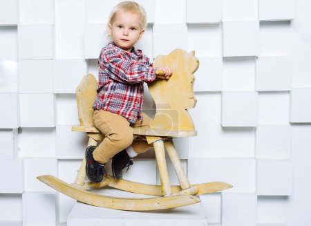 Téléchargez les photos : Beau petit enfant chevauchant sur le cheval jouet. Heureuses émotions franches. Plan studio
. - en image libre de droit