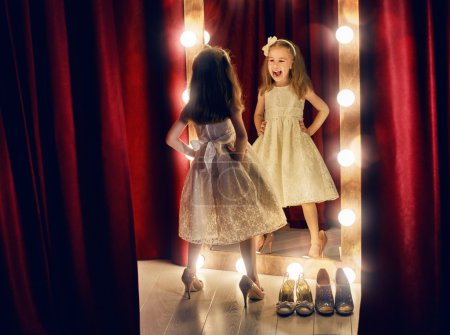 Photo for Cute little fashionista. Happy child girl try on outfits and mom's shoes looking at mirror. - Royalty Free Image