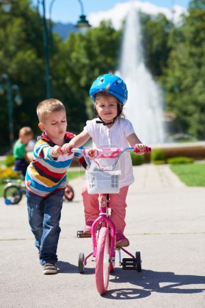 Boy and girl in park learning to ride a bike