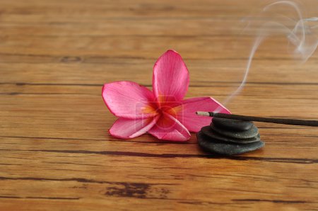 Téléchargez les photos : Une fleur de frangipani rose affichée avec une pile de cailloux et des bâtons d'encens brûlants - en image libre de droit