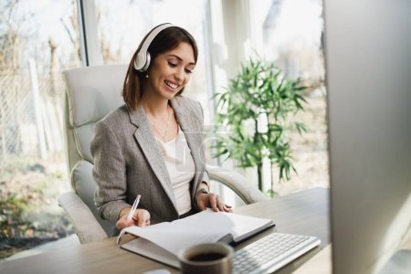 Eine attraktive junge Frau mit Kopfhörern arbeitet zu Hause am Computer.