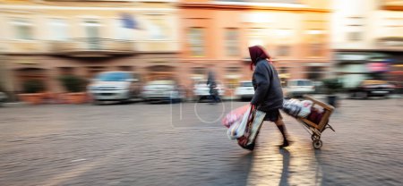 Imagen abstracta de personas en la calle con un fondo borroso. Desenfoque intencional del movimiento. Una anciana arrastra un carro con sus pertenencias
