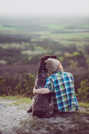 Frau und Hund posieren im Freien. Mädchen liebt und umarmt ihren Hund und beobachtet die Landschaft.