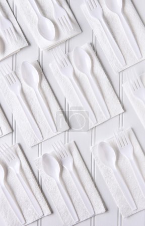 Téléchargez les photos : Vue de dessus des serviettes blanches avec fourchettes et cuillères en plastique blanc sur une table blanche. Format vertical
. - en image libre de droit