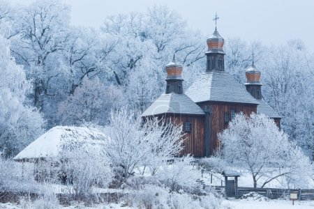 Foto de Una antigua iglesia de madera entre los árboles en la nieve - Imagen libre de derechos