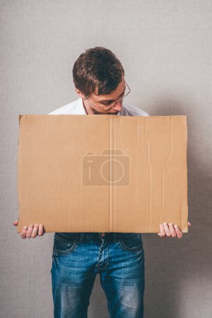 Photo for Young man holding a cardboard banner against a grey background - Royalty Free Image