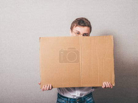 Photo for Young man holding a cardboard banner against a grey background - Royalty Free Image