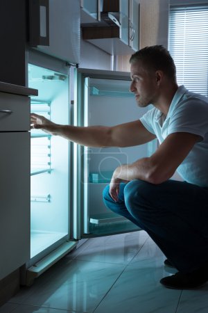 Hombre sentado frente al refrigerador vacío
