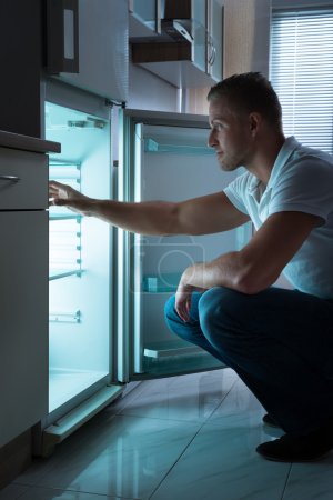 Téléchargez les photos : Jeune homme assis devant un réfrigérateur vide la nuit - en image libre de droit