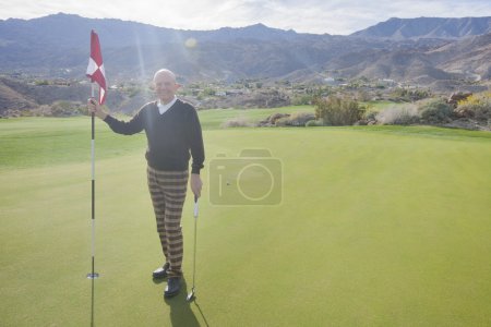 Photo for Happy senior male golfer holding flag and putter on golf course - Royalty Free Image