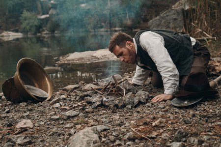 creuseur d'or non rasé makin feu près du lac avec rive rocheuse
