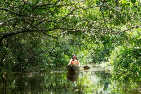 Foto de Hombre adulto indígena en canoa de madera típica cortada de un solo árbol navegando aguas turbias de la selva primaria amazónica ecuatoriana - Imagen libre de derechos