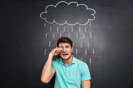 Unhappy disappointed young man crying under the drawn rain