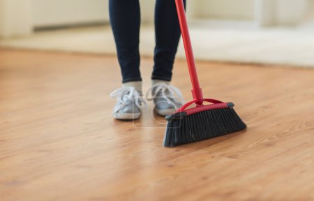 close up of woman legs with broom sweeping floor