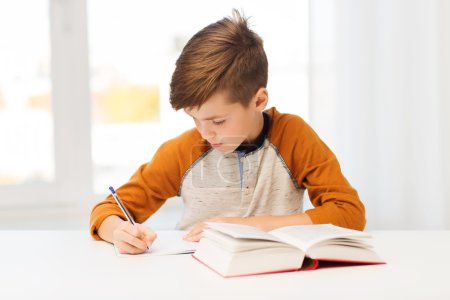 student boy with book writing to notebook at home