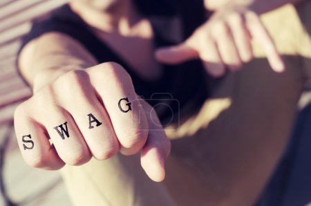 Photo for Closeup of a young man showing his fist with the word swag tattooed in his knuckles, with a filter effect - Royalty Free Image