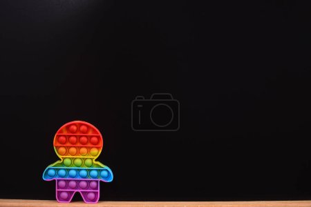 color pop it juguete en la forma de un hombre. sobre una tabla de madera sobre un fondo negro. espacio de copia. juguete anti-estrés