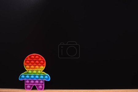 Photo for Color pop it toy in the form of a man. on a wooden board on a black background. copy space. anti-stress toy - Royalty Free Image