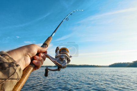 Téléchargez les photos : Pêche sur un lac au lever du soleil. Canne à pêche avec une bobine à la main
. - en image libre de droit