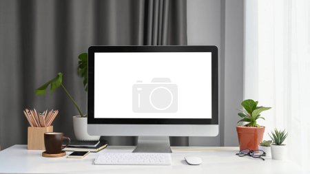 Vista frontal de la computadora simulada con pantalla en blanco, planta de la casa y suministros de oficina en escritorio de oficina blanco.