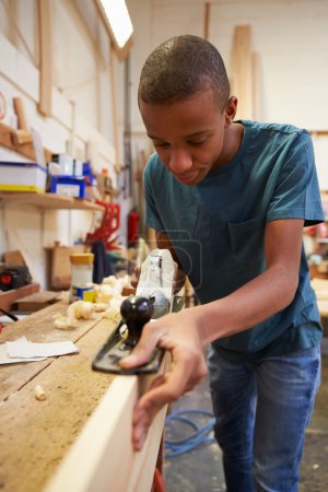 Apprenti rabotage du bois en atelier
