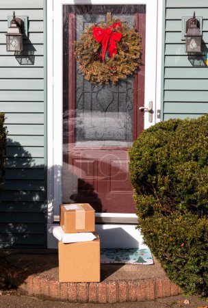 Packages delivered to front door of a residential house with a wreath hanging close to the Christmas holiday.