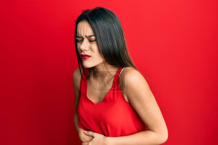 Jeune fille hispanique portant un style décontracté avec chemise sans manches avec la main sur le ventre parce que l'indigestion, la maladie douloureuse se sent mal. concept de douleur. 