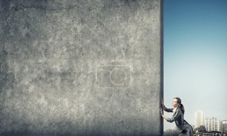 Téléchargez les photos : Jeune femme d'affaires faisant des efforts pour déplacer mur de ciment - en image libre de droit