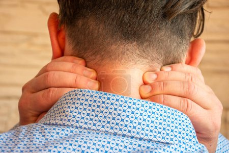 Concept photo of soreness of back of neck, muscle pain, numbness loss of sensitivity of skin in anatomical area. Patient holds himself with both hands behind neck in case of pain syndrome cervicalgia