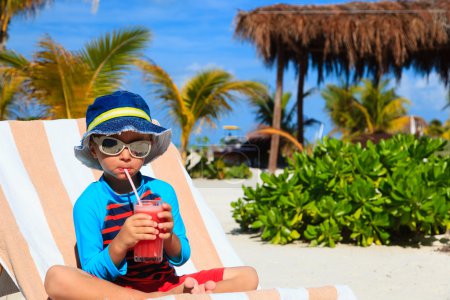 lindo niño bebiendo jugo en la playa
