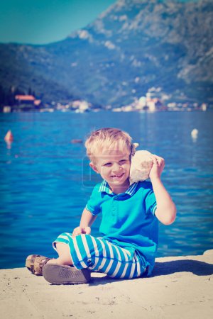 niño feliz escuchando concha marina en la playa
