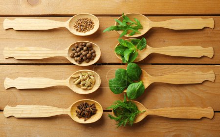 Cucharas de madera con hierbas frescas y especias sobre fondo de madera
