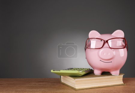 Photo for Piggy bank in glasses with calculator and book on grey background - Royalty Free Image