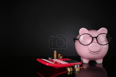 Hucha en vasos con calculadora y monedas sobre fondo oscuro
