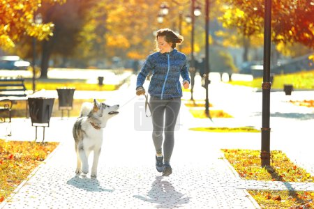 Téléchargez les photos : Joyeux jeune femme jogging avec son chien dans le parc - en image libre de droit