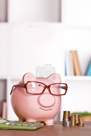 Photo for Piggy bank in glasses with calculator and coins on home or office background - Royalty Free Image