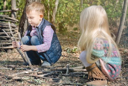 Téléchargez les photos : Deux jeunes enfants, un petit garçon et une fille aux cheveux blonds, accroupis sur le sol jouant avec des bâtons à l'extérieur - en image libre de droit