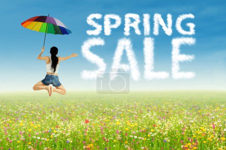 Photo for A girl with umbrella jumping beside of spring sale clouds - Royalty Free Image