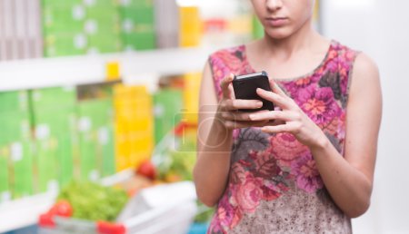 Photo for Unrecognizable woman at store using smartphone with shelves on background. - Royalty Free Image