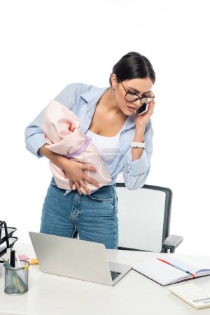 young mother talking on cellphone while holding baby near work desk isolated on white