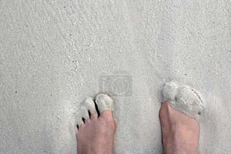 Füße in den Sand stecken. Eine Frau genießt es, mit den Füßen im warmen weichen Sandstrand zu stehen