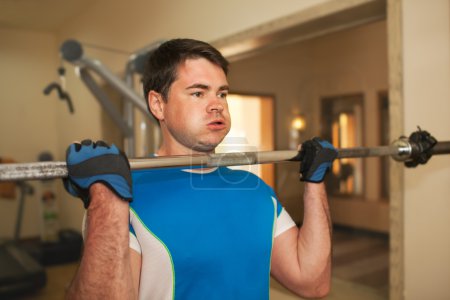 Téléchargez les photos : Jeune homme faisant renforcer l'exercice dans la salle de gym. Il soulève haltère sans disques de poids - en image libre de droit