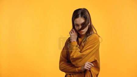 teenager in sweater with pouting lips looking at camera while adjusting hair isolated on yellow