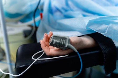 Mano de un paciente acostado en la mesa de operaciones. Sensor de oxímetro de pulso en el dedo. El paciente está durmiendo bajo anestesia general..