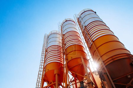 Silos de cemento de fábrica de planta de cemento por lotes contra el sol de la tarde con cielo azul claro Silos de cemento de fábrica de planta de cemento por lotes contra el sol de la tarde con cielo azul claro