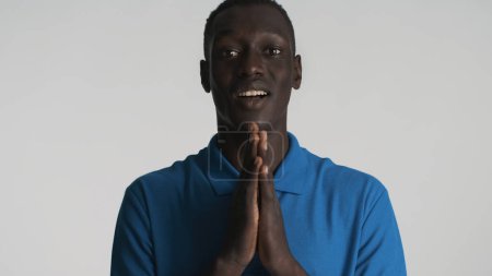 Emocionado chico afroamericano mantener plam presionado juntos buscando inspirado sobre fondo blanco
