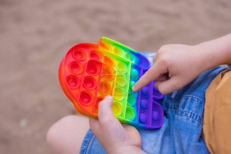 Juguete sensorial colorido antiestrés nervioso empuje pop en las manos de los niños pequeños. Antiestrés de moda pop it toy. Arco iris nerviosa sensorial. Nuevo juguete de silicona de moda.