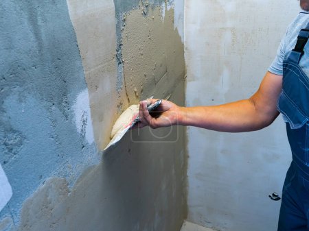 Mejora de la casa por trabajador. Mano con una espátula. Paletas de trabajo masilla en la pared con acabado masilla